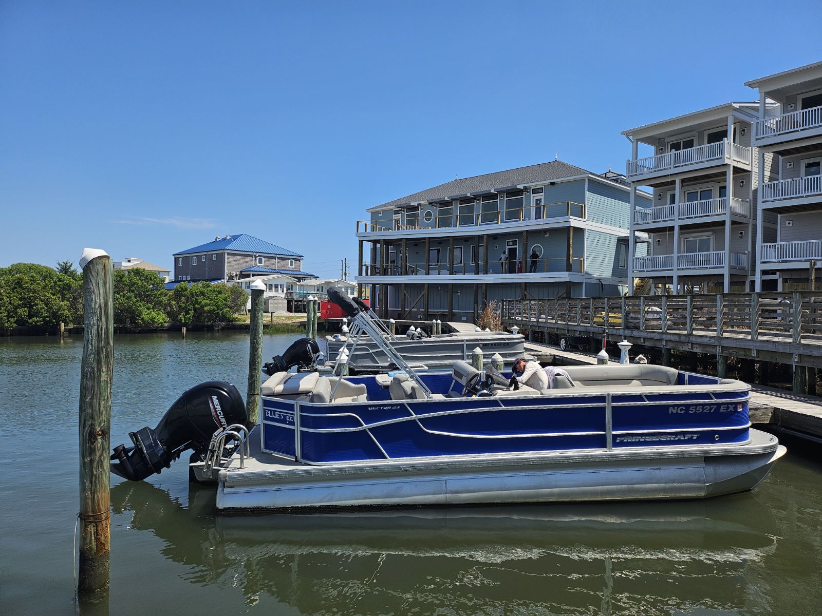 Blue pontoon boat docked at coastal marina with waterfront building — 4th of July in Surf City NC