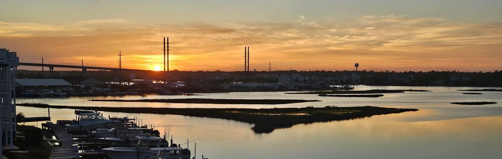 Fiery orange sunset over marsh and boat slips with skyline silhouette — sunset at Marina Joe's
