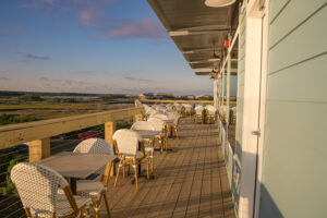 Expansive upper-level outdoor deck with woven bistro chairs and marsh views at golden hour at Marina Joe's in Surf City, the answer to where to take dad for Father's Day at Topsail Island