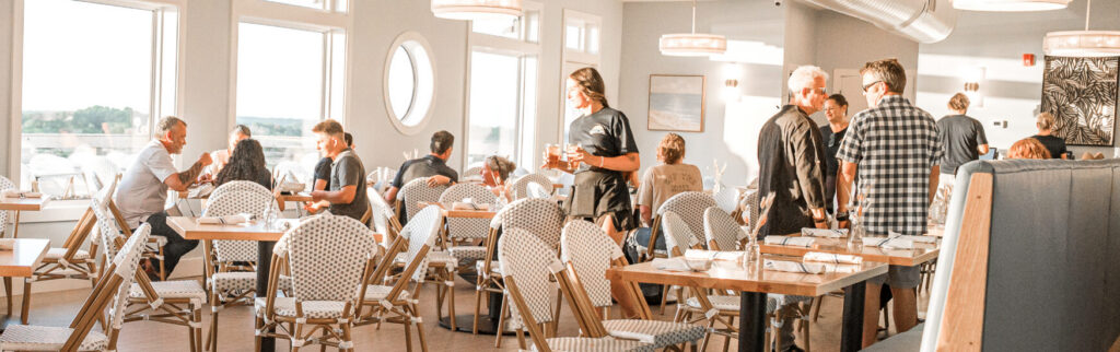 Sunlit coastal restaurant dining room with panoramic waterway windows and guests dining — Marina Joe's private parties