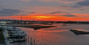 Golden hour Intracoastal Waterway marina at sunset with white boats docked at wooden piers and vibrant orange sky.